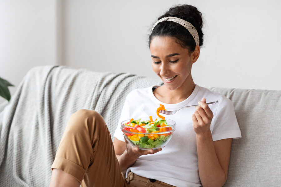 A similing woman sitting on her sofa eating a salad