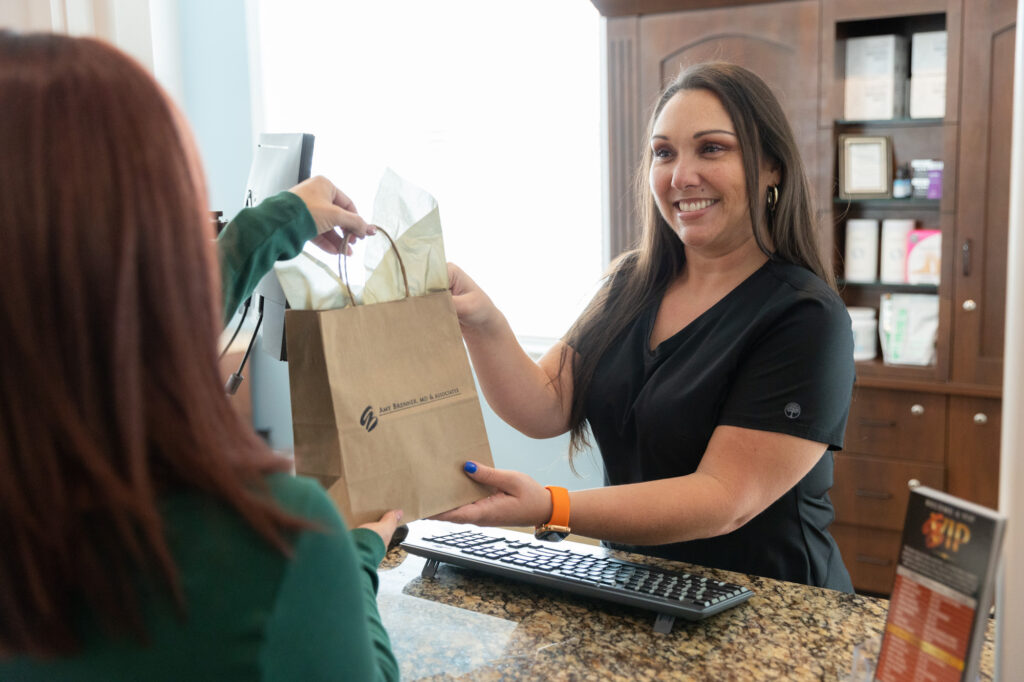 A team member at Amy Brenner, MD & Associates passing a branded bag to a patient who just learned how to prevent acne.