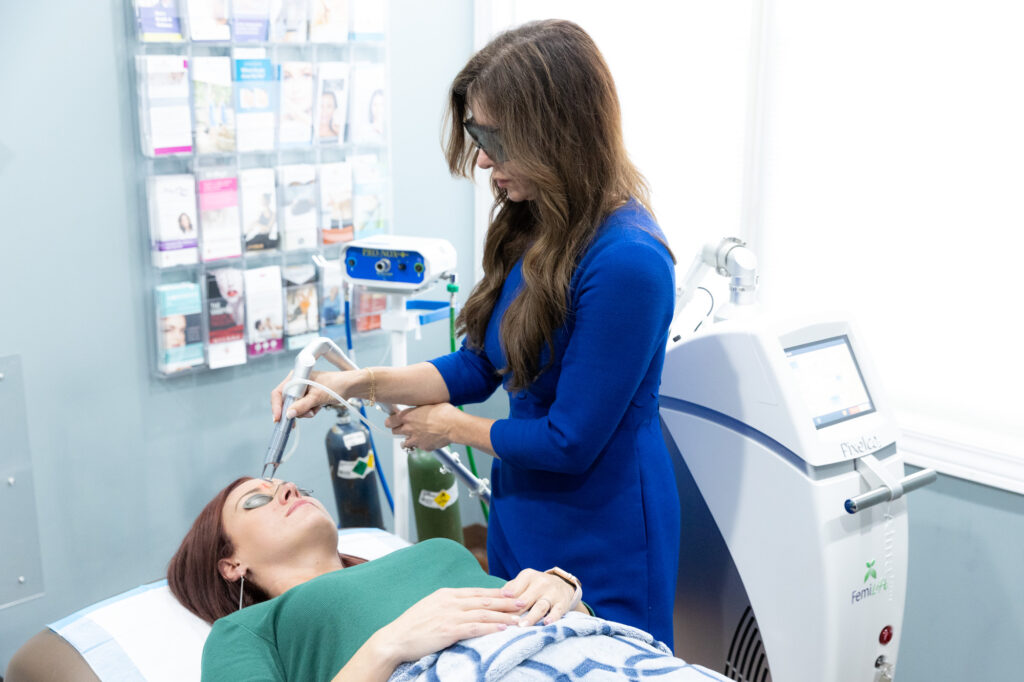 Dr. Amy Brenner performing a Pixel CO2 spot treatment for dark spots in a treatment room on a woman lying down and wearing glasses.