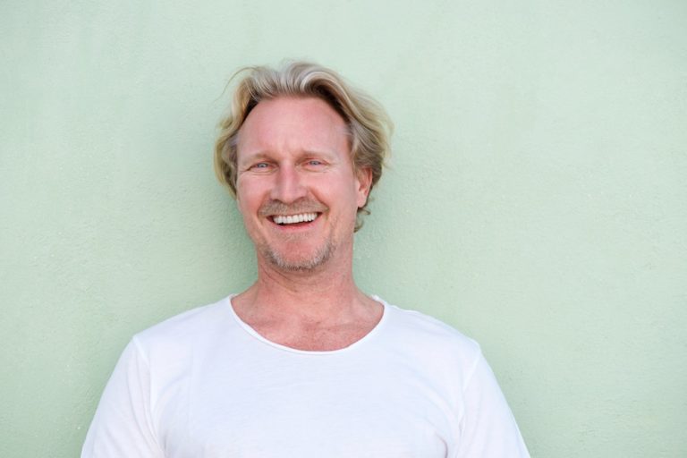 middle aged male HRT patient in white long sleeved t shirt smiling against a green background