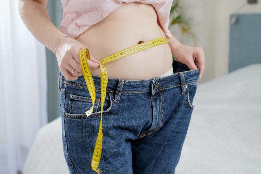 Woman measuring her slim waist and holding pants that are too big after using peptides for weight loss.