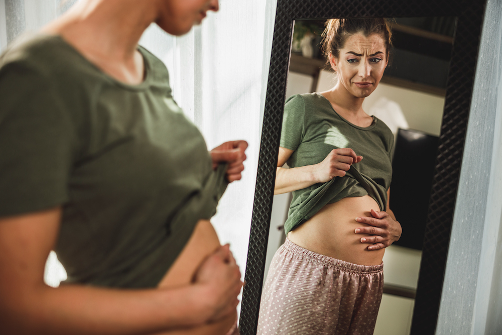 Unhappy woman touching her belly and wondering "Why am I always bloated?"