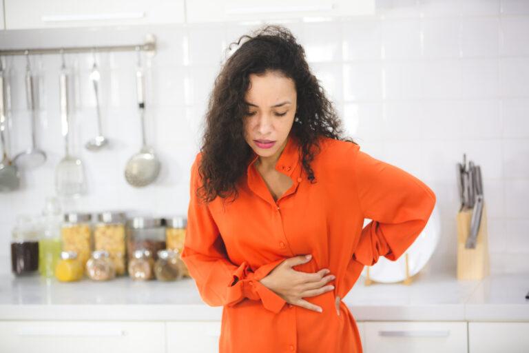 Woman standing in a kitchen and holding her stomach in pain before leaky gut testing in Cincinnati.