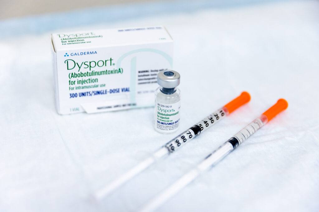 A box and vial of Dysport in Mason, OH, next to syringes, all lying on a white table.