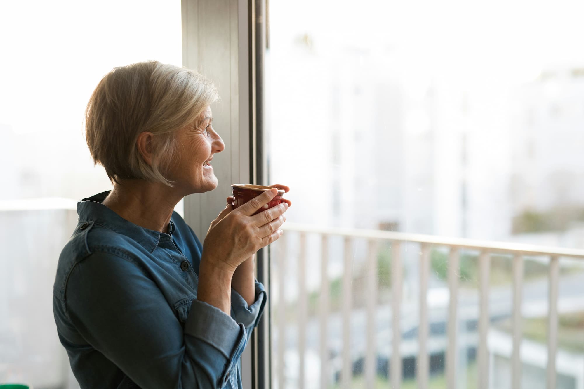 An older woman enjoying a cup of coffee and looking out the window, reflecting on her menopause treatment in Cincinnati