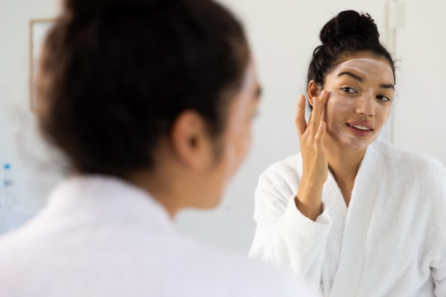 A woman applying her new skincare product in the mirror after learning how to prevent acne.