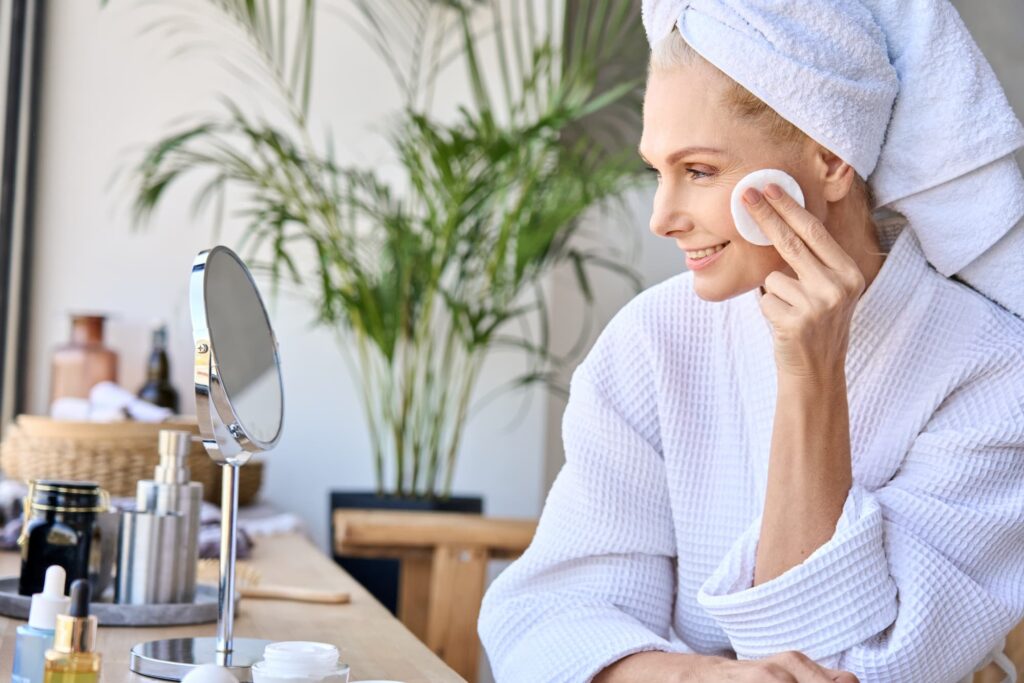 A mature woman sitting in her bathrobe, applying the best skin care products in Cincinnati.