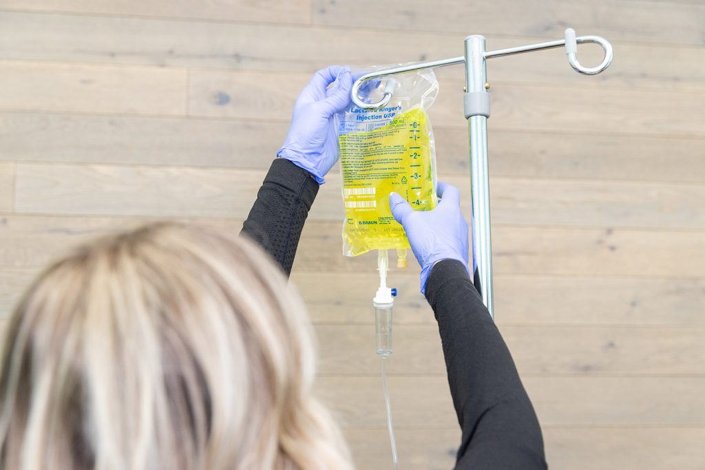 Close up of a woman wearing gloves setting up a fluid bag at an IV clinic in Cincinnati.