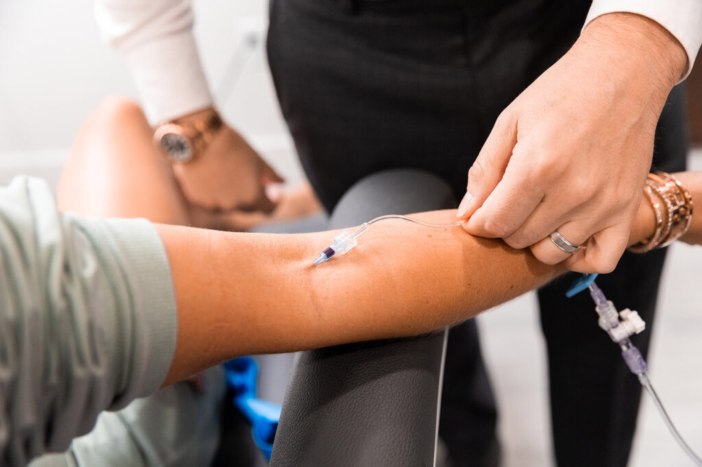 A needle for IV infusion in Cincinnati placed in an outstretched arm as another person checks on the IV tube.