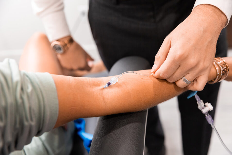 A needle for IV infusion in Cincinnati placed in an outstretched arm as another person checks on the IV tube.