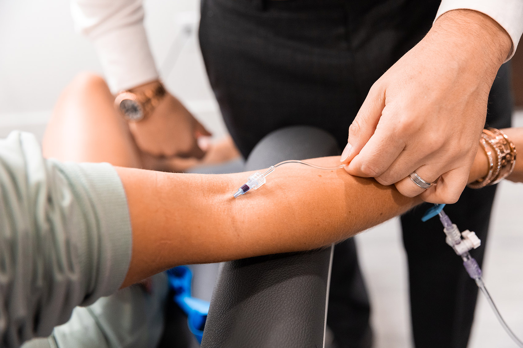 A needle for IV infusion in Cincinnati placed in an outstretched arm as another person checks on the IV tube.