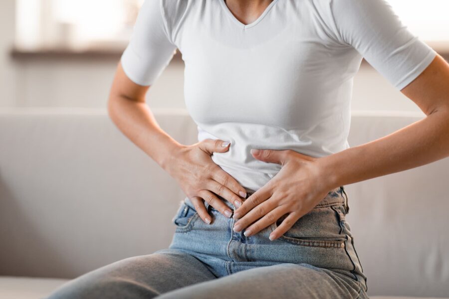 A woman from the neck down, sitting on a couch and clutching her stomach because she needs help with her gut health in Cincinnati.
