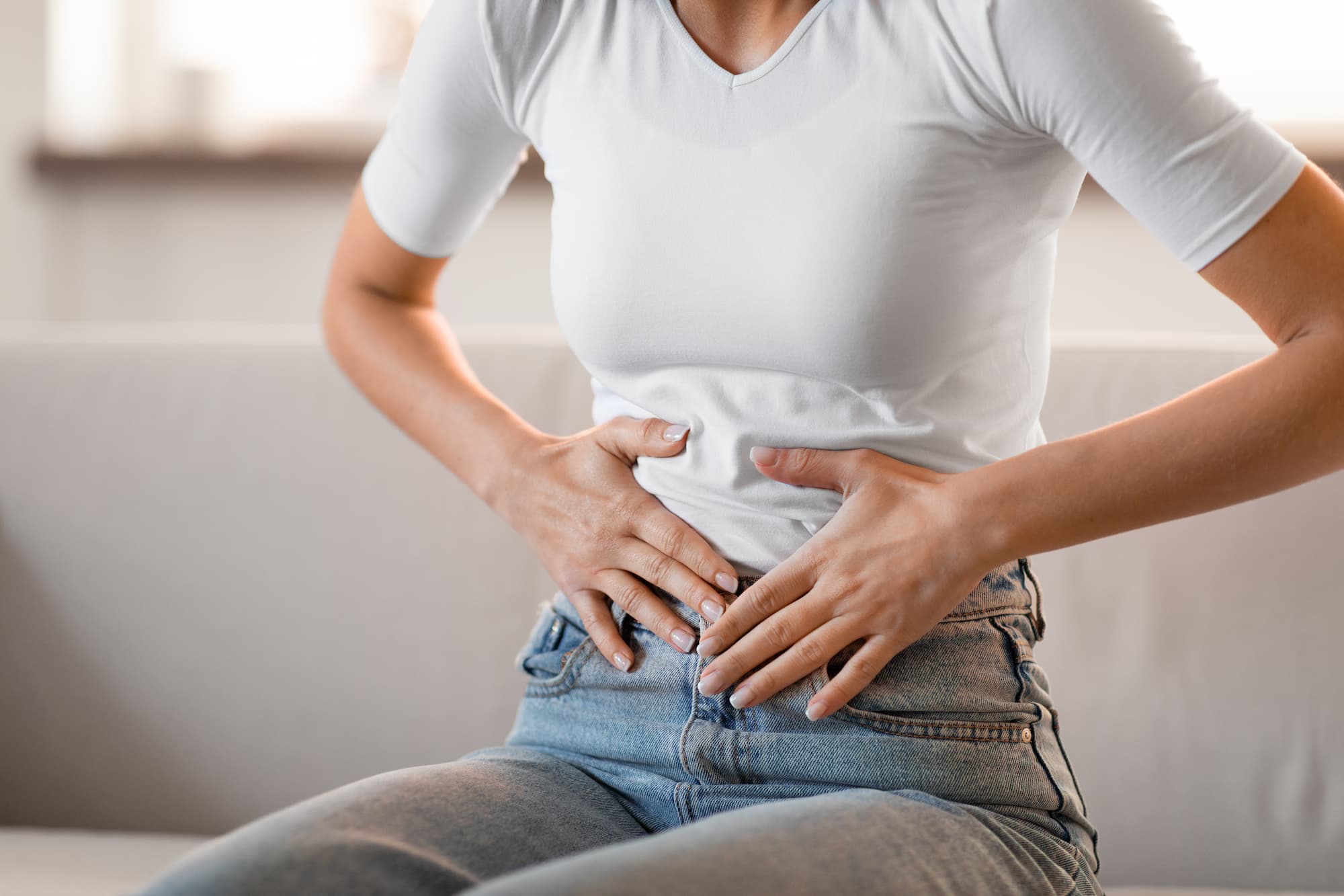 A woman from the neck down, sitting on a couch and clutching her stomach because she needs help with her gut health in Cincinnati.
