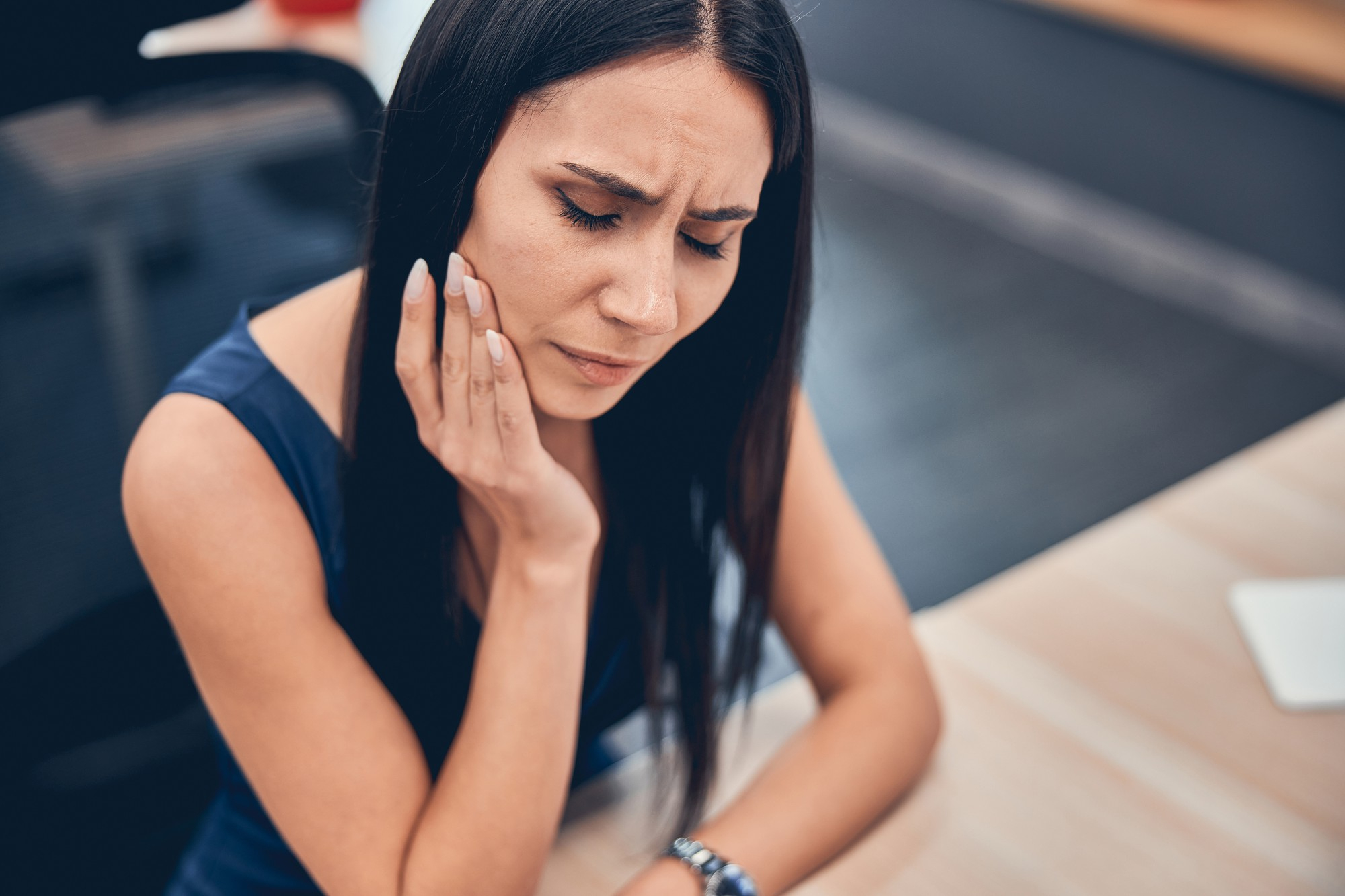 Woman sitting at desk and placing her hand on her jaw to try and ease pain. To find relief, she could visit Amy Brenner, MD & Associates for Botox for TMJ in Cincinnati.